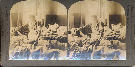 Stereo card view of wounded Belgian soldiers in an Antwerp hospital attended by a Red Cross nurse. The nurse attends to a severely wounded soldier whose head, face, and hands are swathed in bandages.
Text:
V18817—The Horror of War: Ghastly Glimpse of Belgian Wounded, Antwerp Hospital.