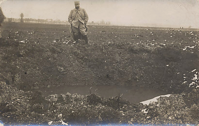 A French soldier wearing the uniform of 1914/1915 stands by the side of a water-filled shell crater.
Text Reverse:
R. Guilleminot, Bœspnug et Cie. - Paris