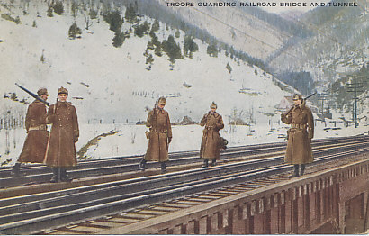 On guard against saboteurs and espionage, troops guard the Boston & Maine Railroad bridge and the Hoosac Tunnel, in Adams, Massachusetts.
Text:
Troops guarding railroad bridge and tunnel
Reverse:
These boys are on guard at the Hoosac Tunnel on the Boston & Maine Railroad in the western part of Massachusetts. Most of the freight from the West passes this tunnel, and the authorities of the state deemed it wise to post guards as a protection against fanatics and spies. The Hoosac Tunnel is the largest and most important in the New England states; it is 4¾ miles long. This precaution, however, is not limited to New England, as most of the railroad bridges, canals, locks, etc., throughout the country have been guarded by regulars or National Guardsmen ever since the declaration of war with Germany.
Photo © International Film Service, Inc.
No 16. Published by American Colortype Co., Chicago
