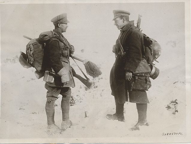 British soldiers on the Western Front in an official photograph dated March 5, 1917.
Text:
British soldiers in full winter equipment discuss the war. British official photograph taken on the Western front showing two fully equipped British Tommies discussing the war and the trend of events at a spot behind the lines. They are carrying considerable equipment for one man. One could almost start at the left and go around in a circle naming the various articles that constitute his outfit. Helmet, pack, bags, bundles, canteen, rifle, not forgetting the long bristle brush. Despite their cumbersome packs, the men are cheerfully happy. 3/5/17